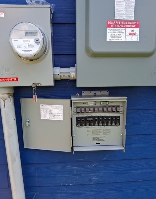 Electrical meter and circuit breaker panel on blue siding.