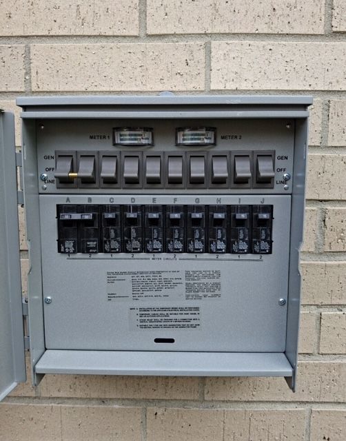 Outdoor electrical panel box with gray cover on brick wall, open, showing breakers.