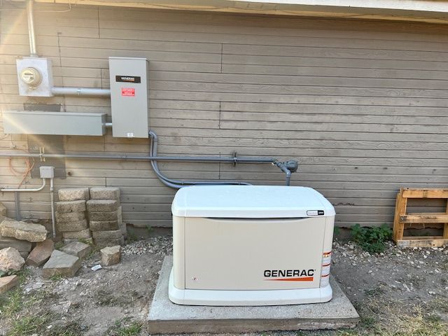 A Generac home generator on a concrete pad, connected to a power panel on a building's exterior wall.
