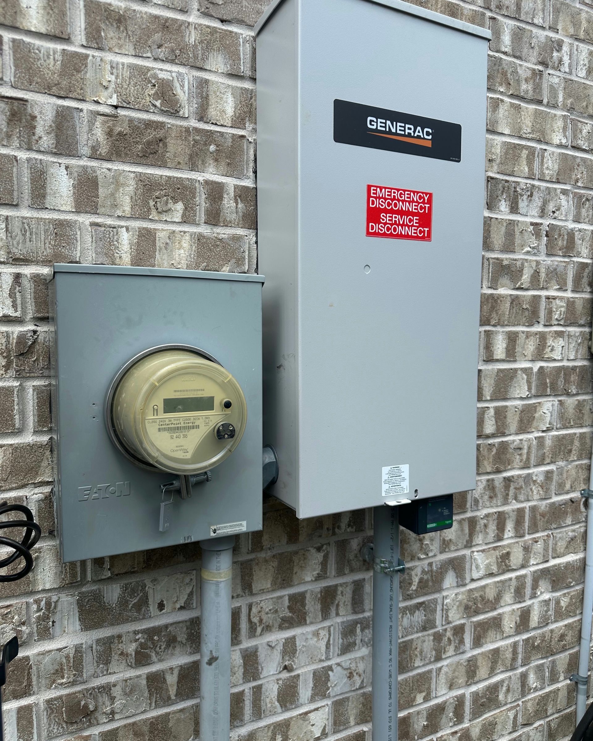 Gray electrical meter and inverter box mounted on a brick wall, connected by conduits.