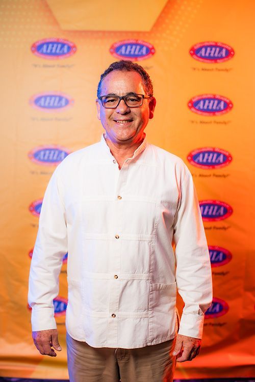Un hombre con gafas y camisa blanca sonríe delante de un fondo con un logotipo.