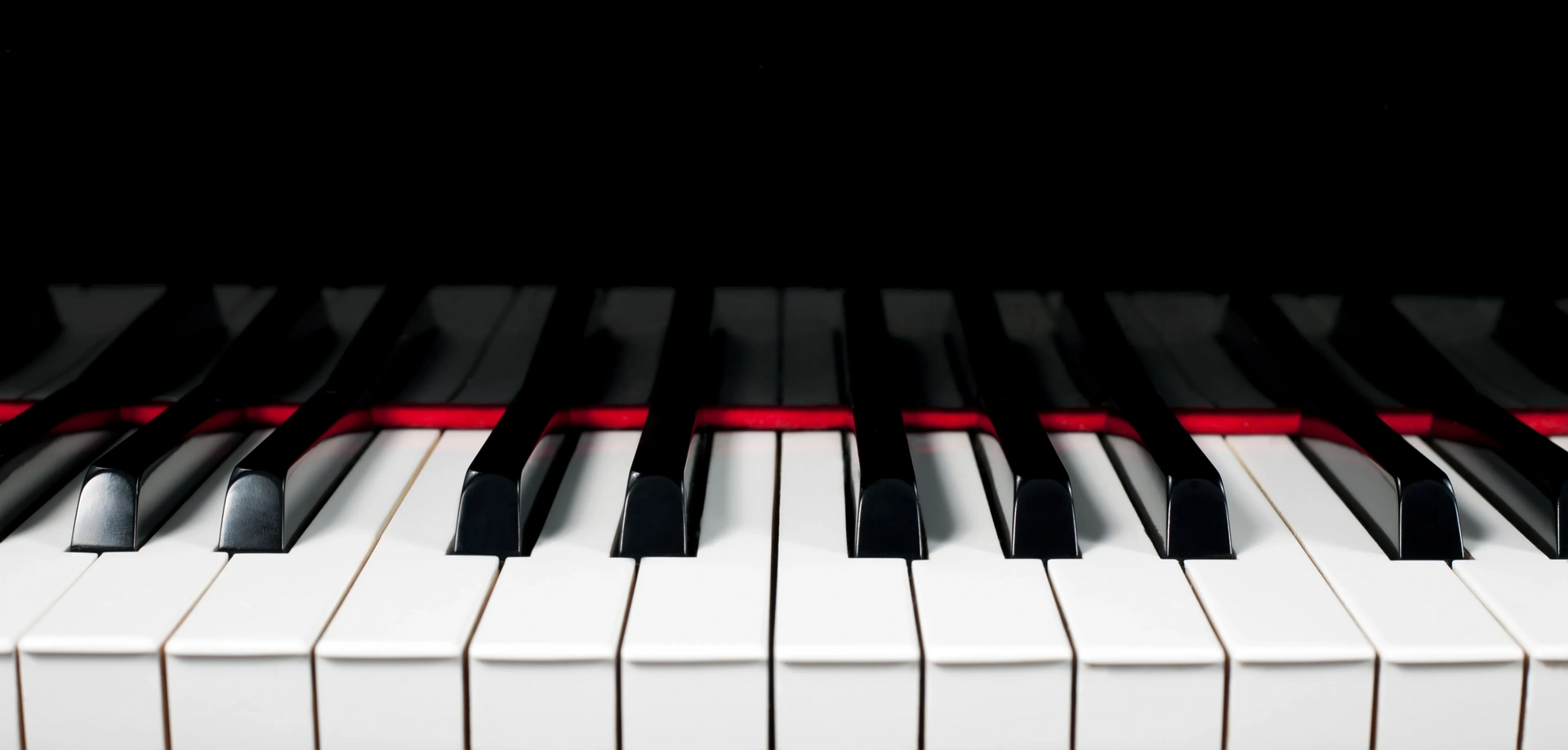 Close-up of piano keys with a red felt strip and dark background
