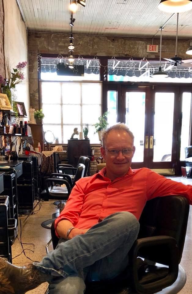 A man in a red shirt is sitting in a chair in a salon.