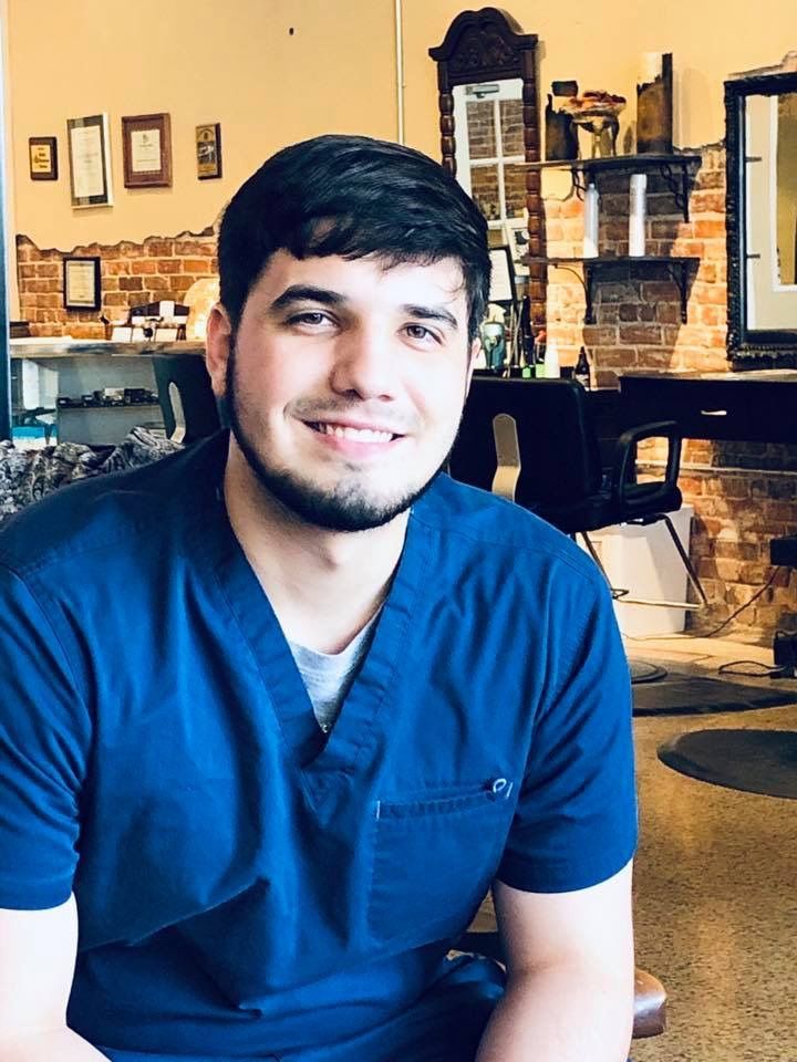 A man in a blue scrub top is smiling in a barber shop