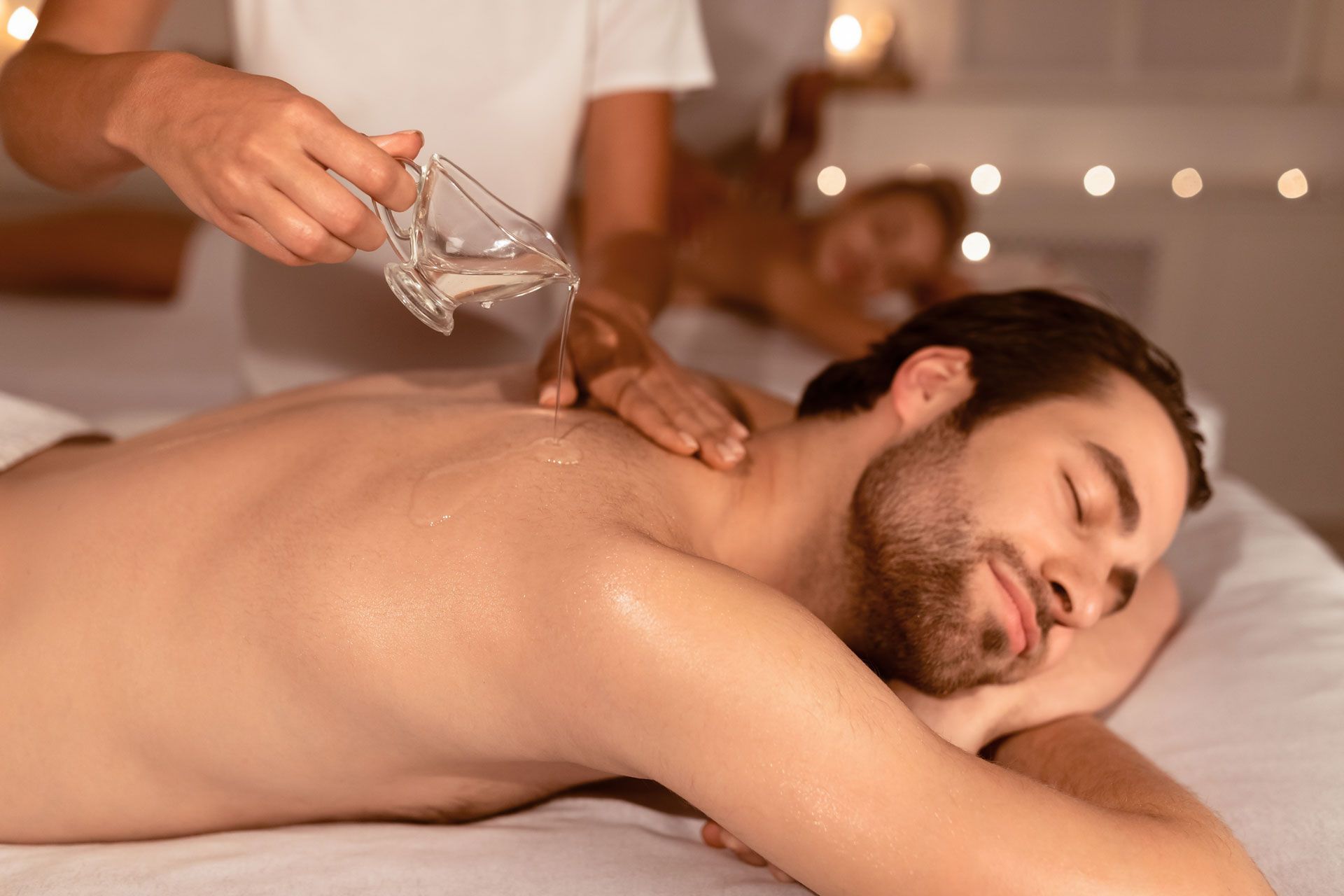 Spa massage with oil being poured onto a man's back as he relaxes face down on a table