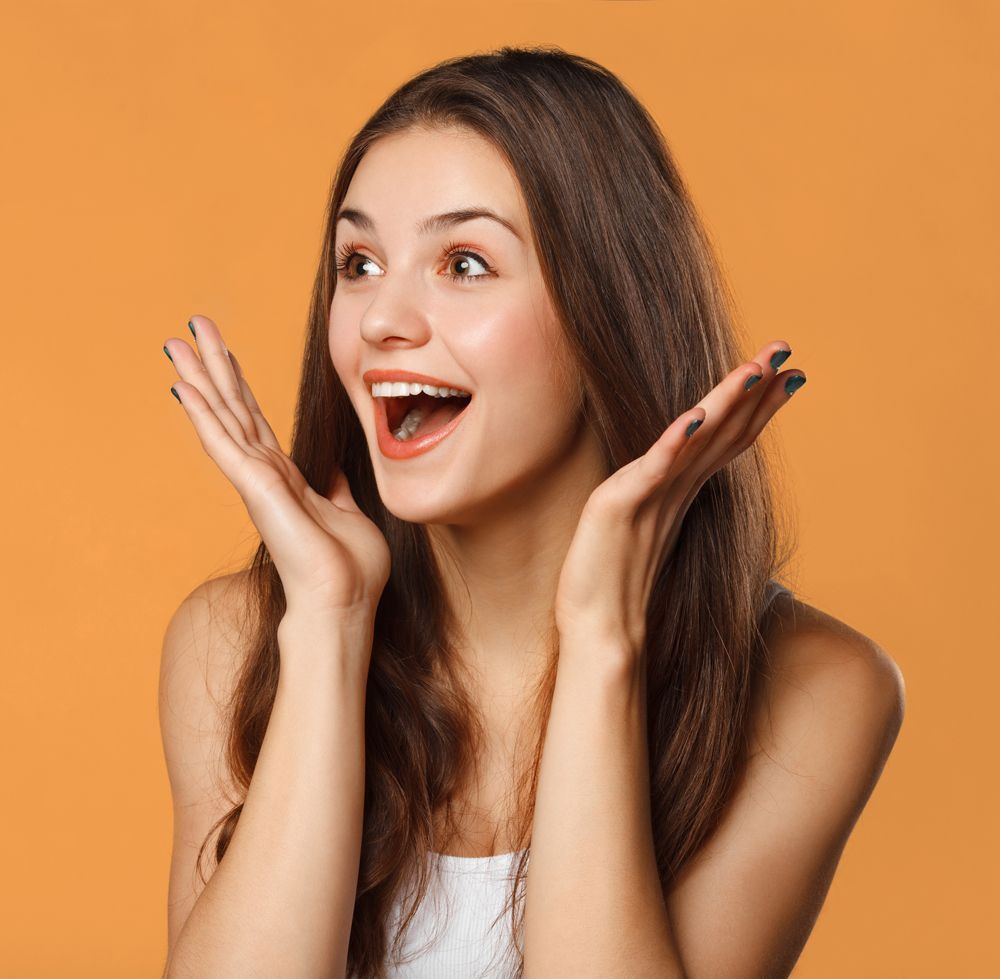 A woman is holding her hands to her face and smiling.