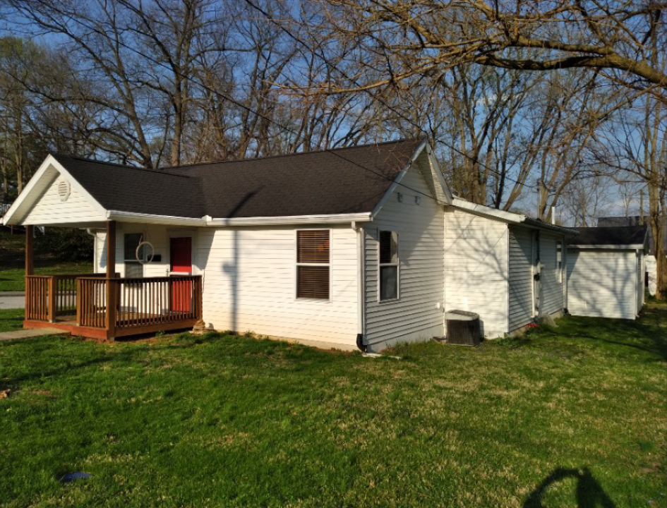 A small white house with a black roof and a porch.