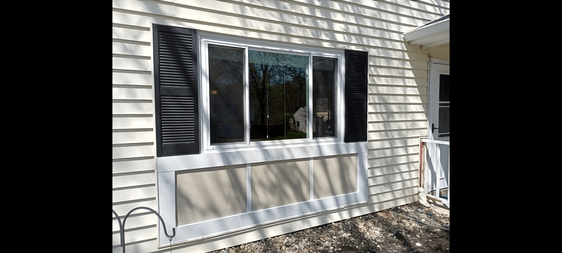 A white house with a large window and black shutters.