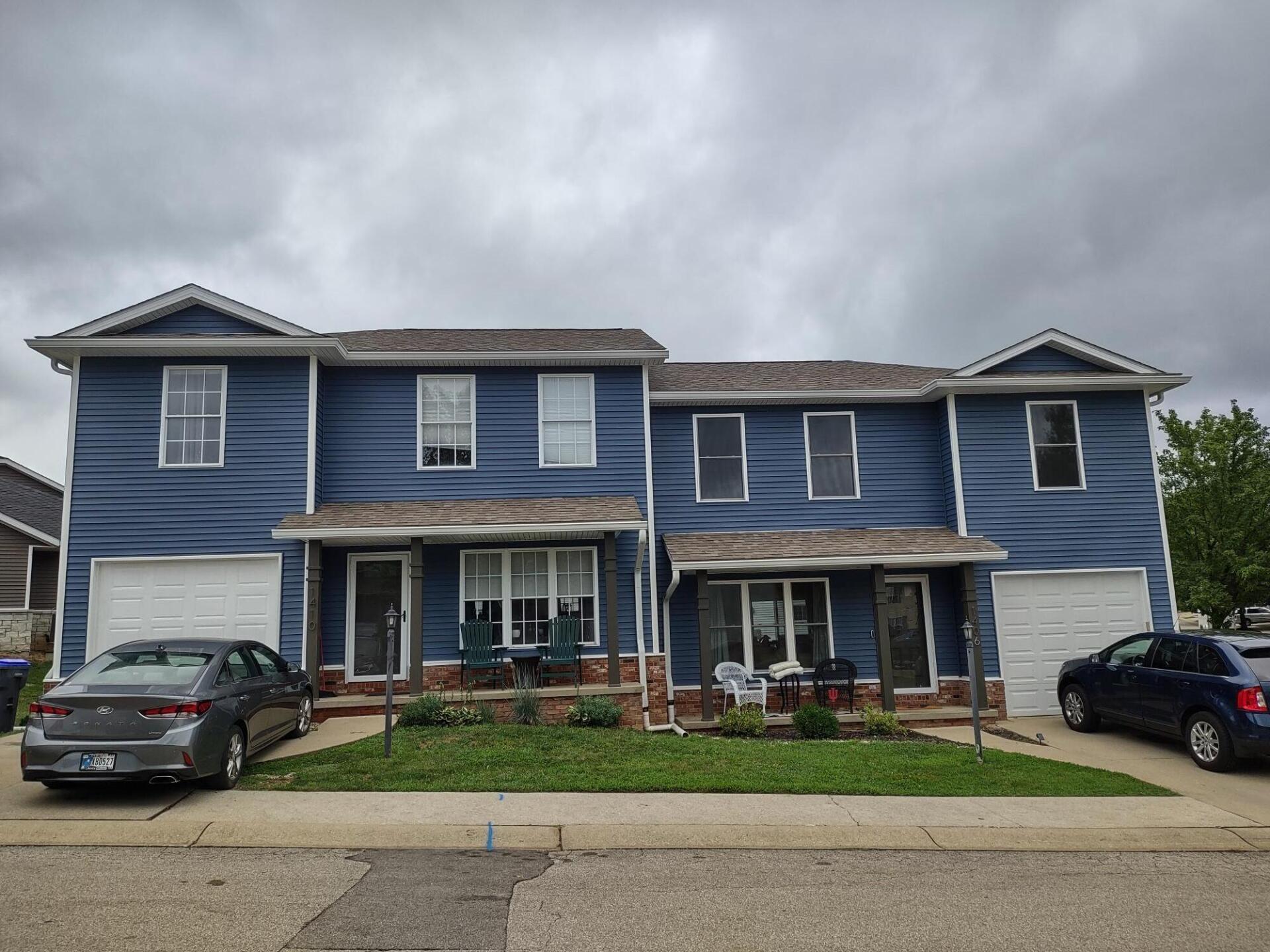 A blue house with two cars parked in front of it on a cloudy day.