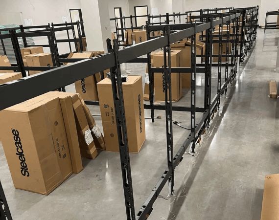 Warehouse aisle with empty black metal shelves and stacked cardboard boxes on the floor
