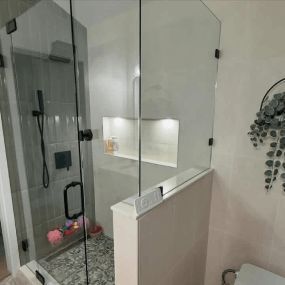 Modern bathroom with glass shower, white vanity, lit mirror, and gray hex tile floor.