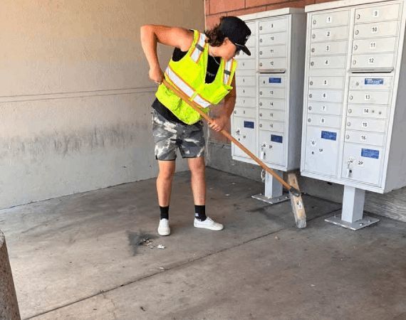Person in a neon vest sweeping a concrete area beside white mailboxes.
