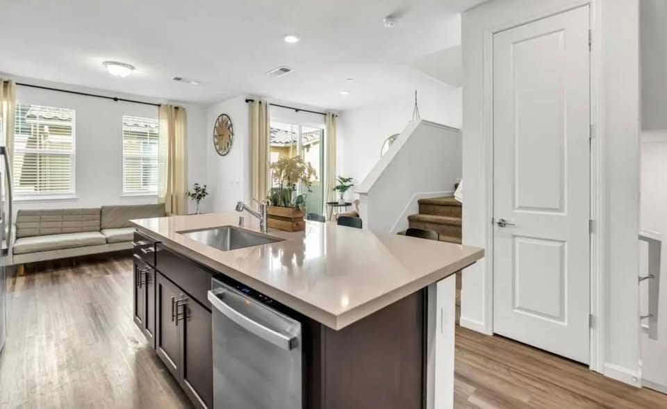 Bright modern kitchen with island, white cabinets, wood floors, and open living area.