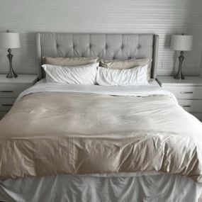 Neatly made bed with white bedding, tufted headboard, and matching bedside lamps in a gray bedroom