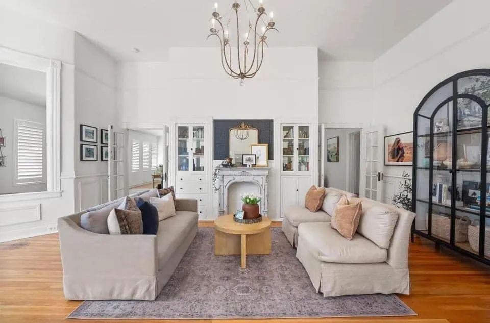 Bright living room with two sofas, fireplace, rug, hardwood floors, and a black arched cabinet