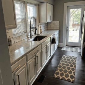 Bright kitchen with white cabinets, black sink, tiled backsplash, and a glass door to a patio.