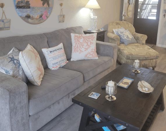 Cozy living room with gray sofa, patterned pillows, chaise chair, and dark coffee table with decor.