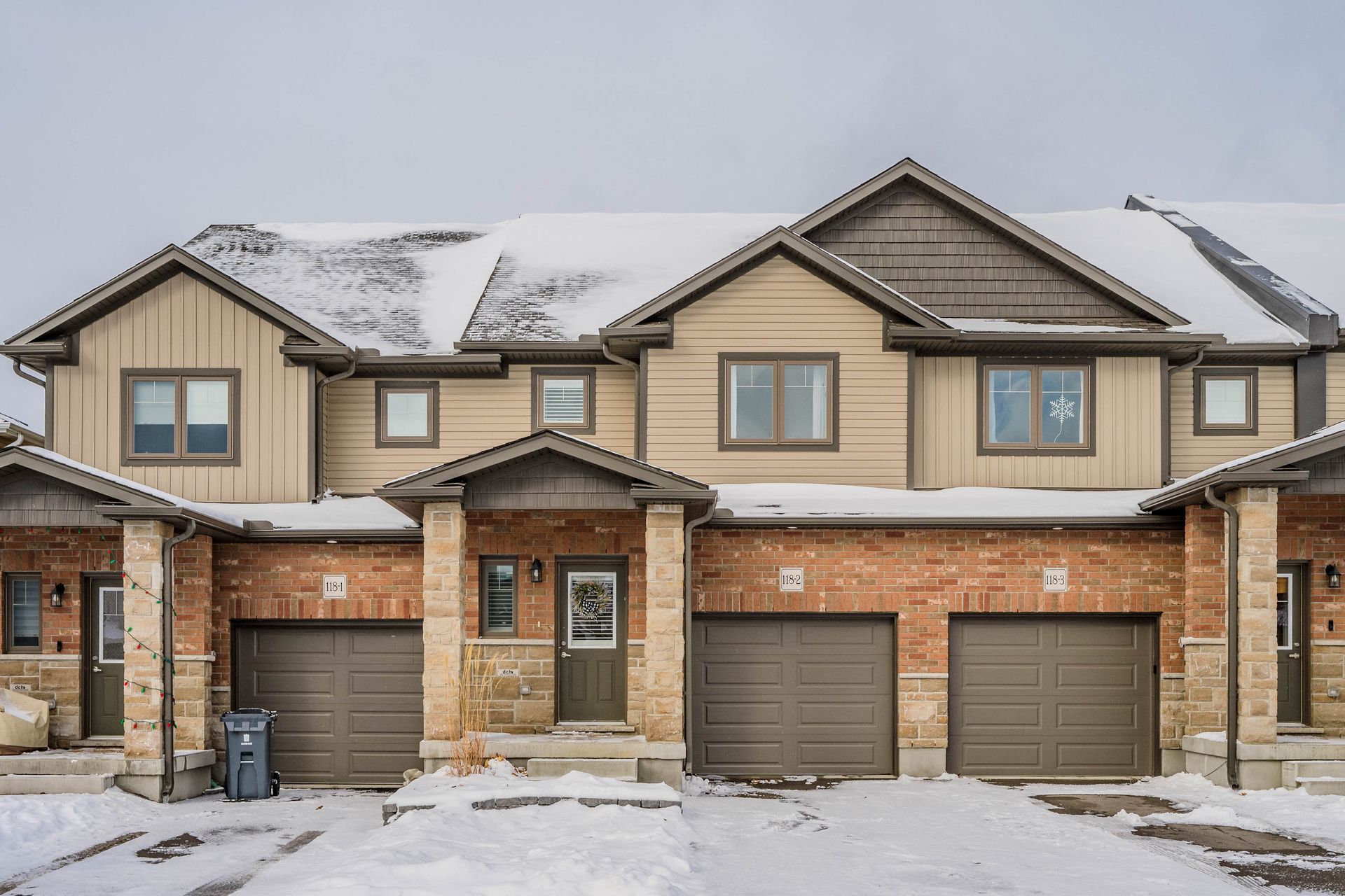 Snow-covered townhouse row with brick facades and attached garages on a winter day