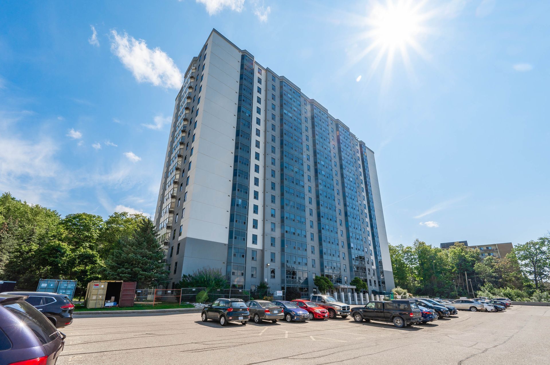Tall modern apartment building with blue glass facade and parked cars under a bright sunny sky