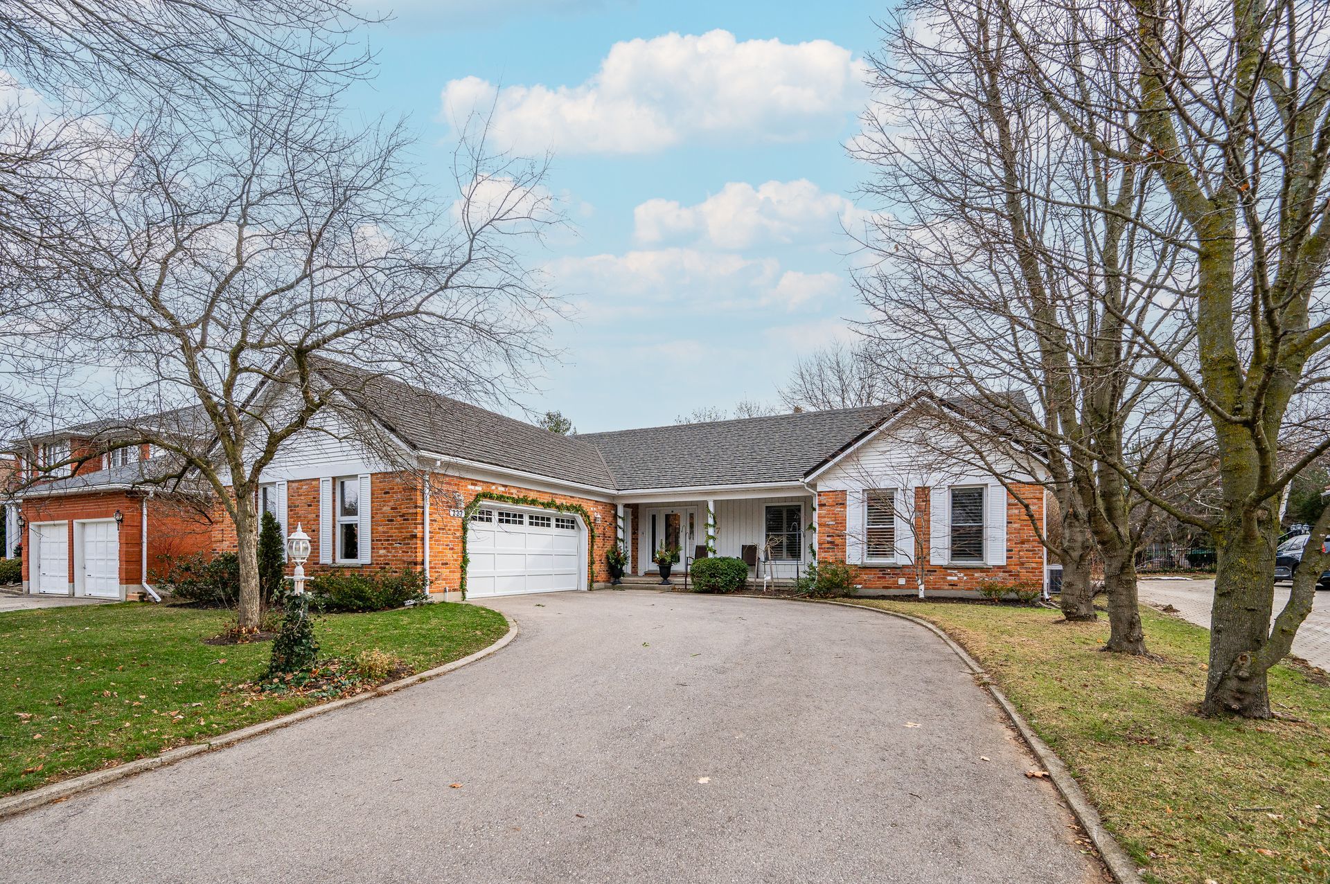 Single-story brick house with a curved driveway, white garage, and bare trees in front yard