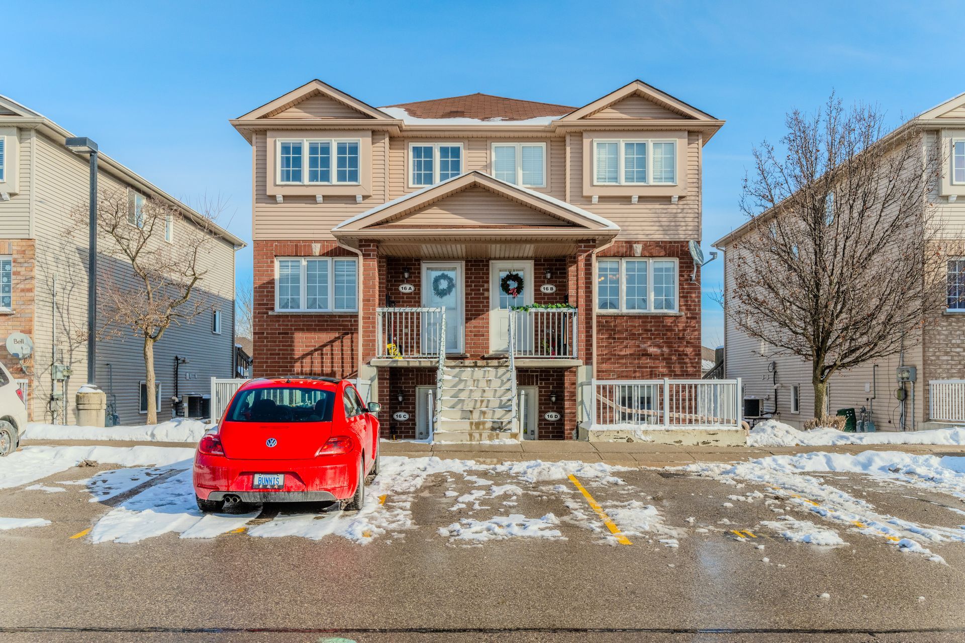 Two-story house with a red car parked in front on a snowy residential street.