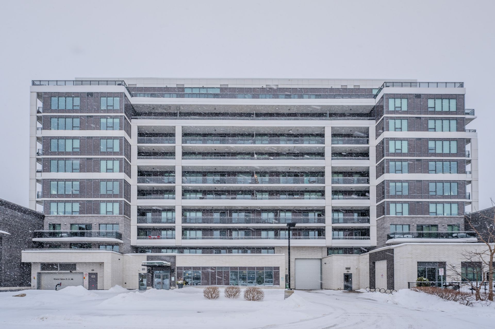 Snow-covered modern apartment building with a central balcony section and two side wings
