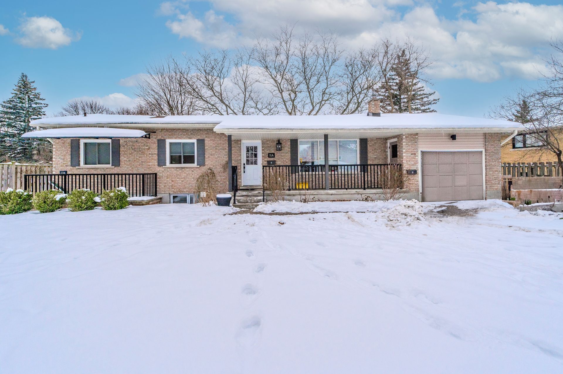 Snow-covered suburban house with attached garage and front porch, seen from the front lawn