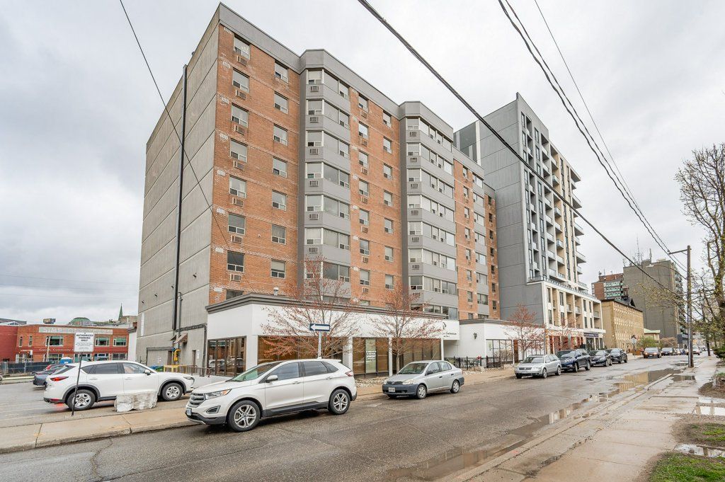 Snowy urban street with parked cars beside tall apartment buildings under an overcast sky