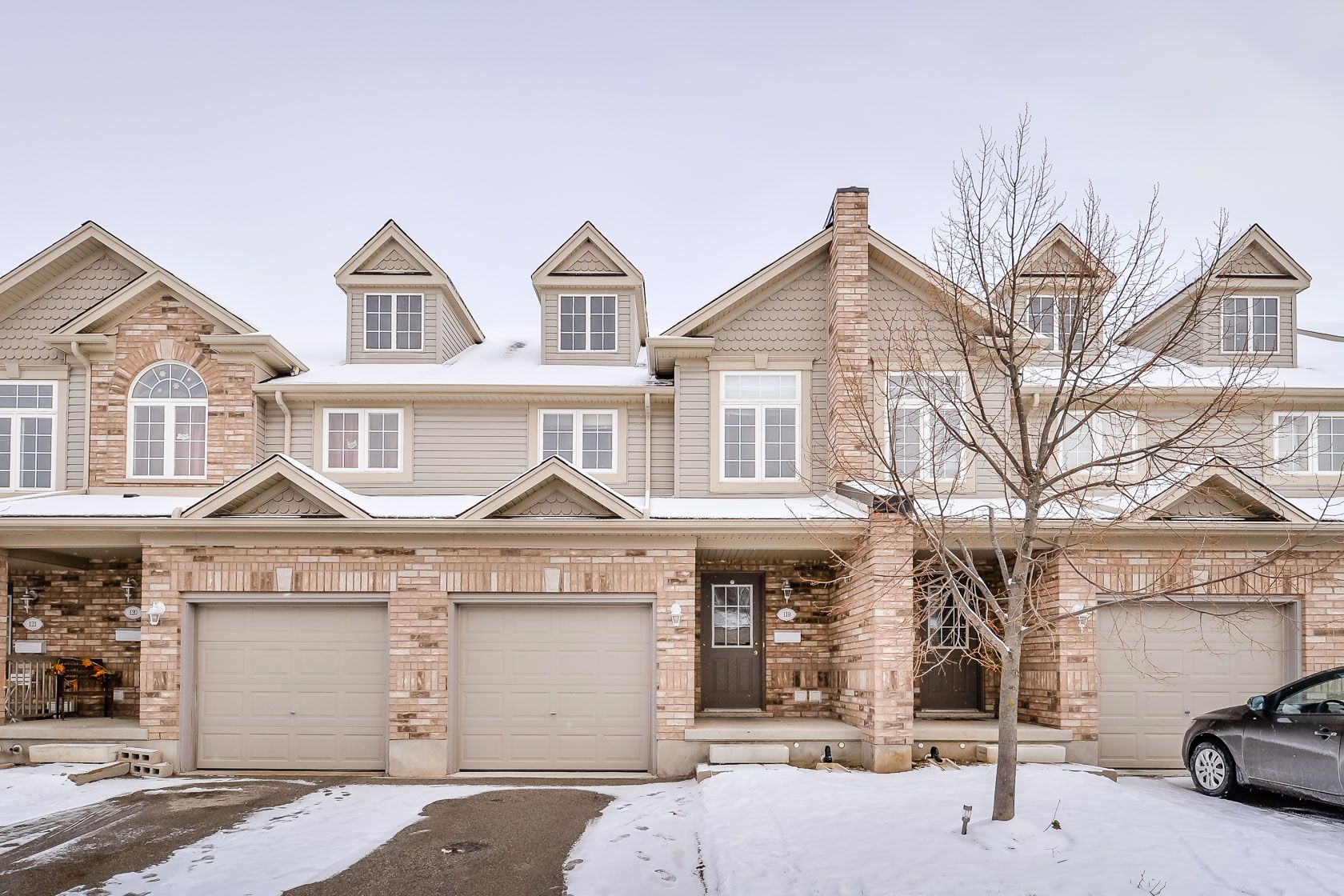 Snowy row of beige townhouses with garages and leafless trees in front