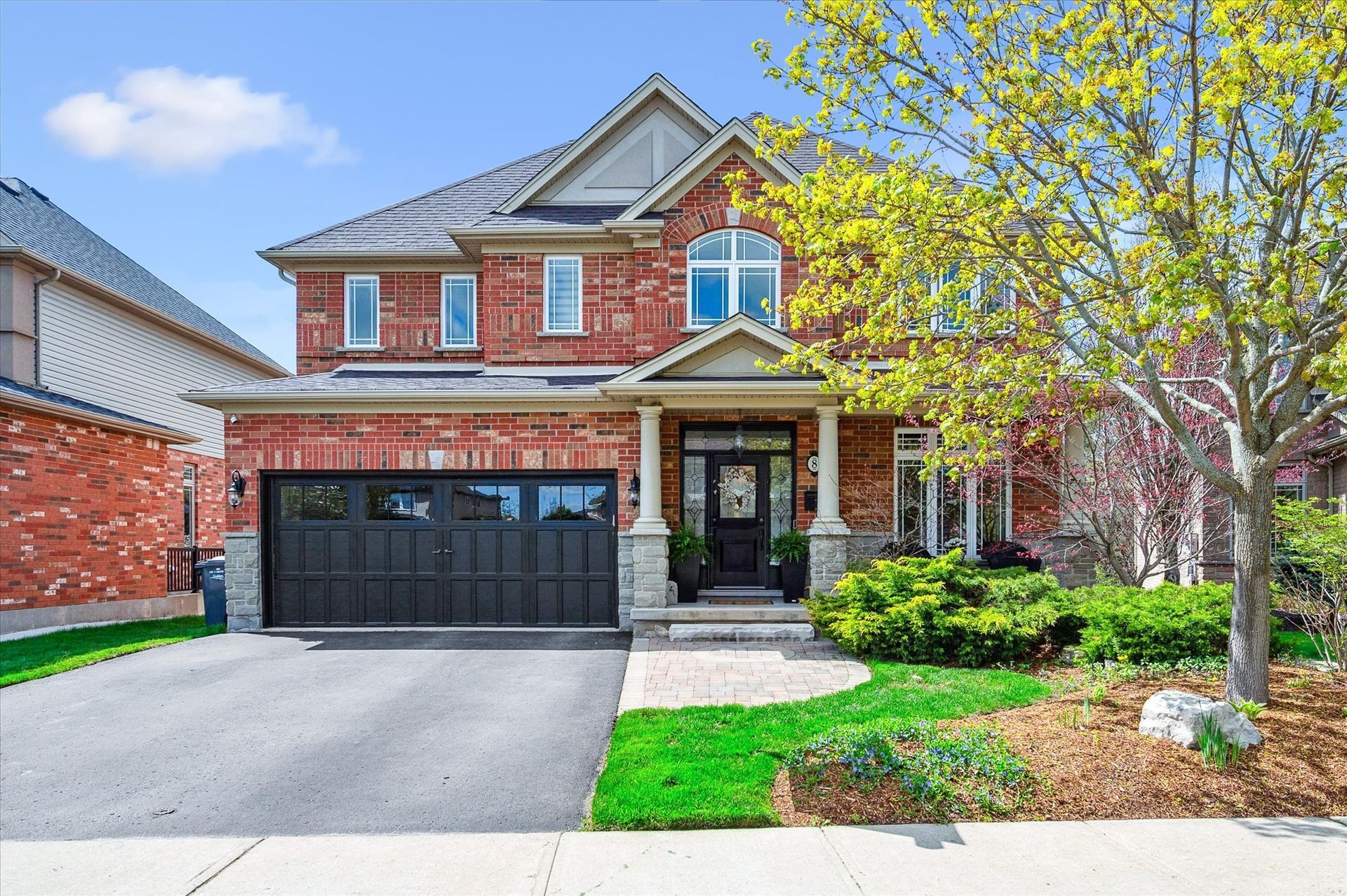 Two-story red brick suburban house with black garage door, driveway, and front lawn