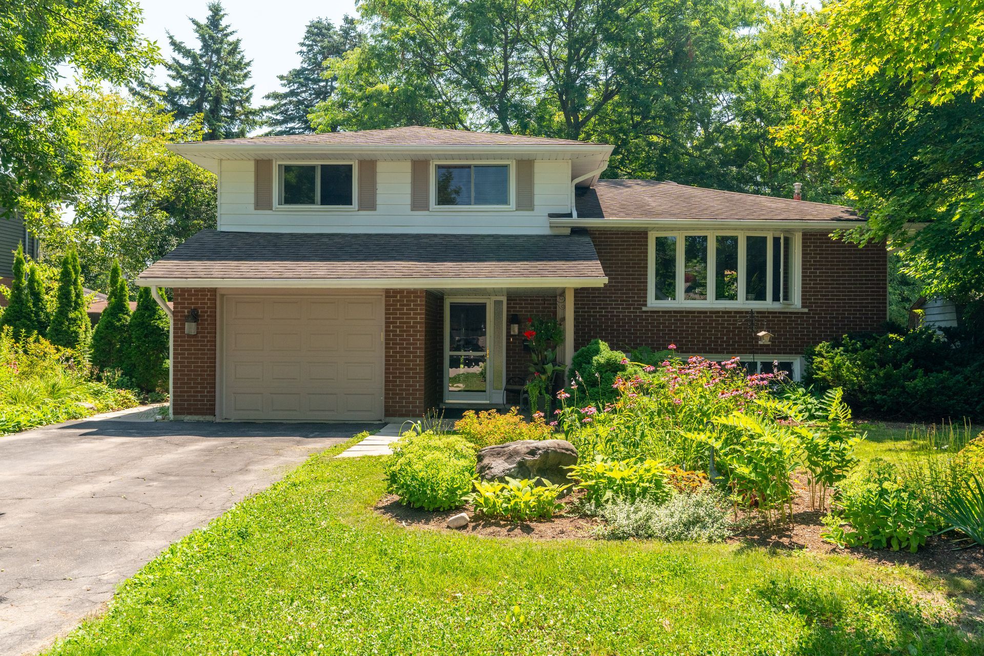 Two-story suburban house with a garage, driveway, and a flower bed in front of a green lawn.