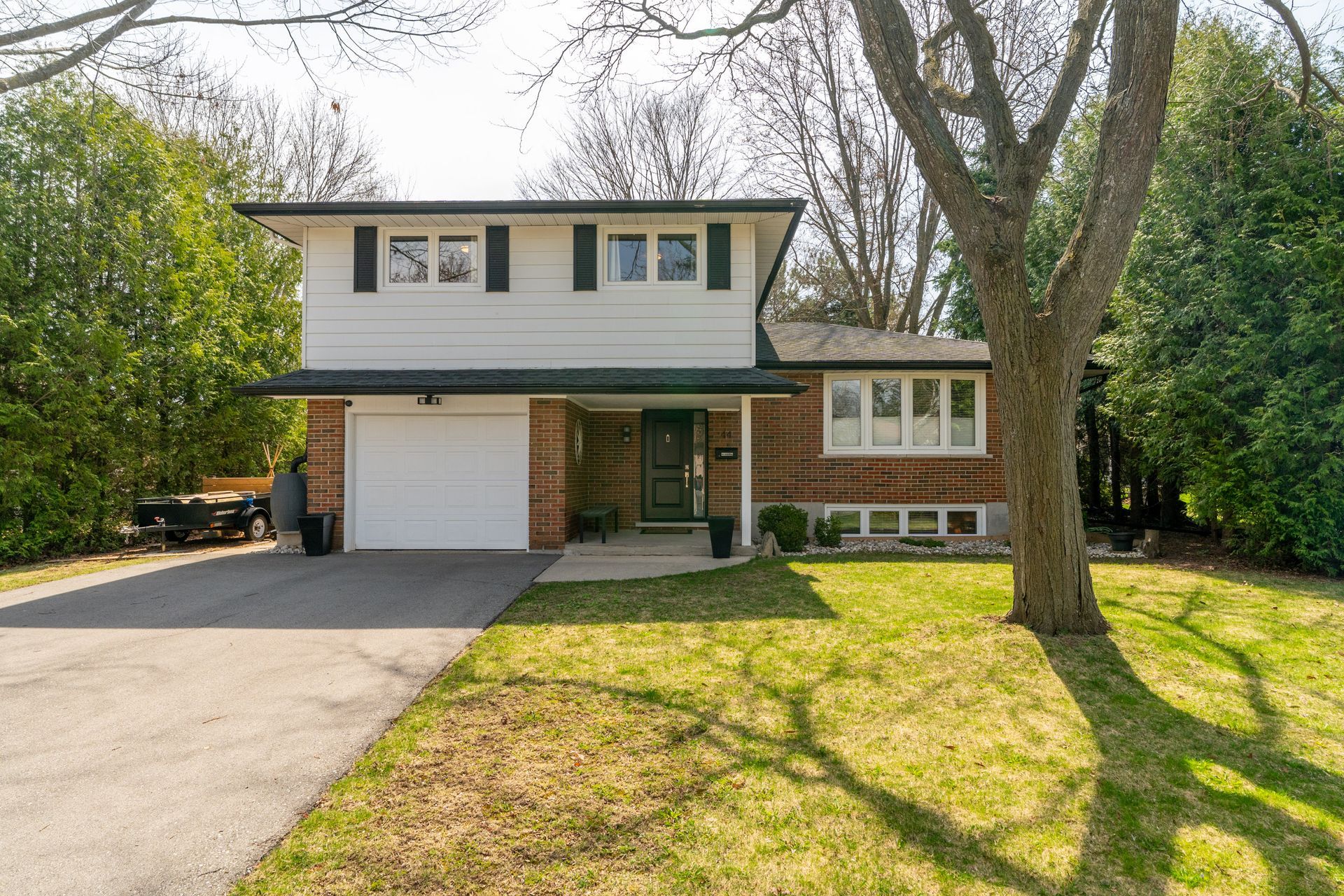 Suburban two-story house with garage, driveway, and front lawn under trees