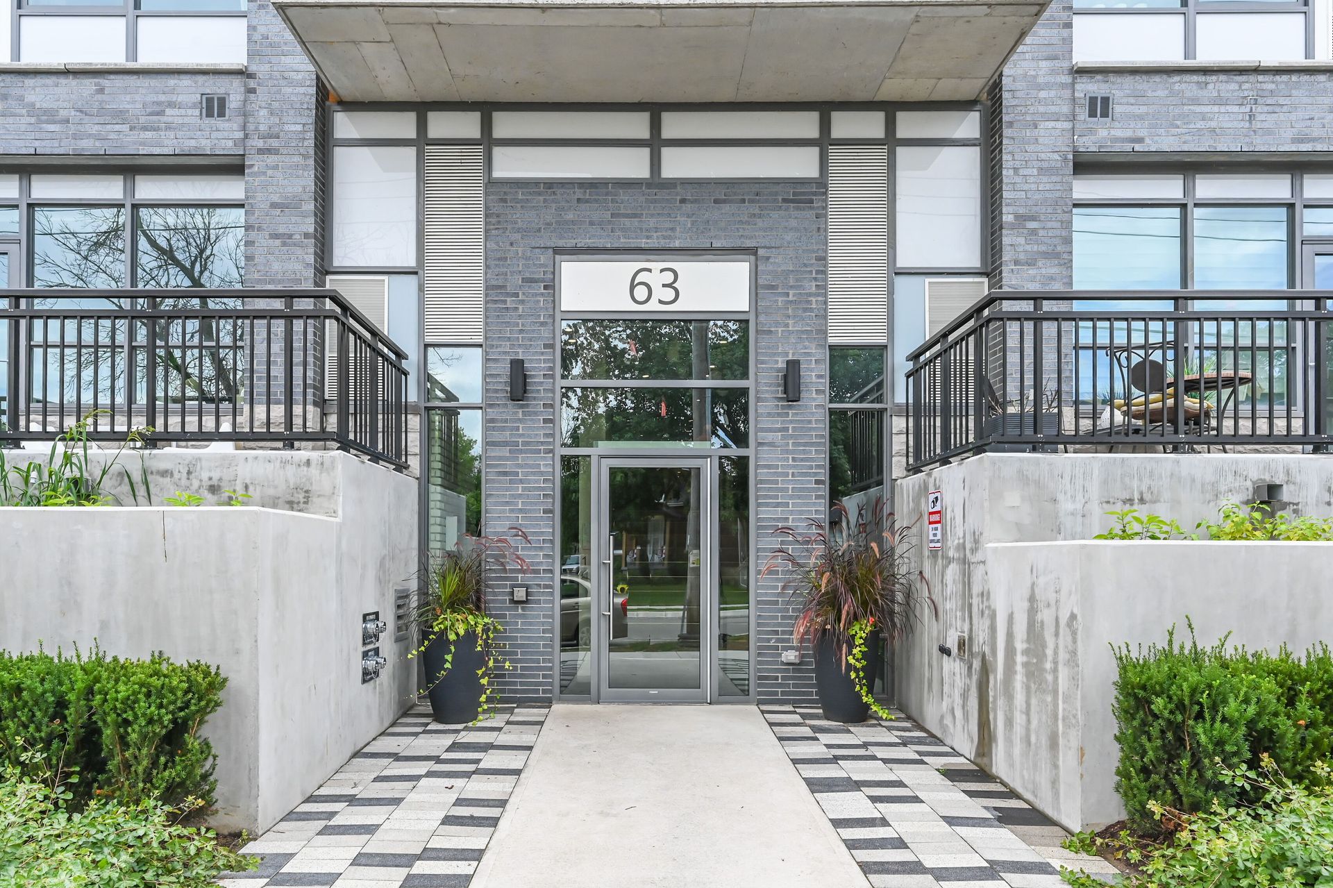 Modern apartment entrance with glass doors, number 63, and a tiled walkway between concrete walls
