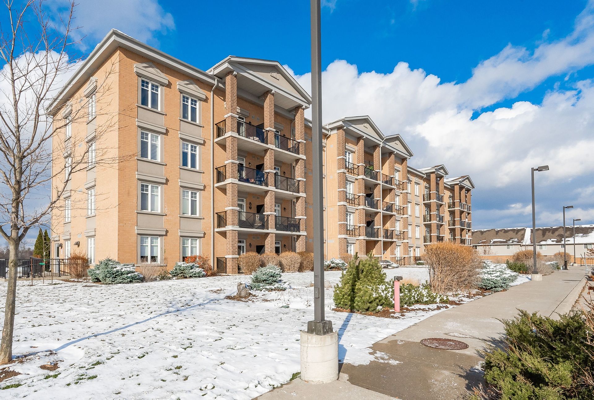 Snowy apartment buildings beside a sidewalk and streetlight under a blue sky