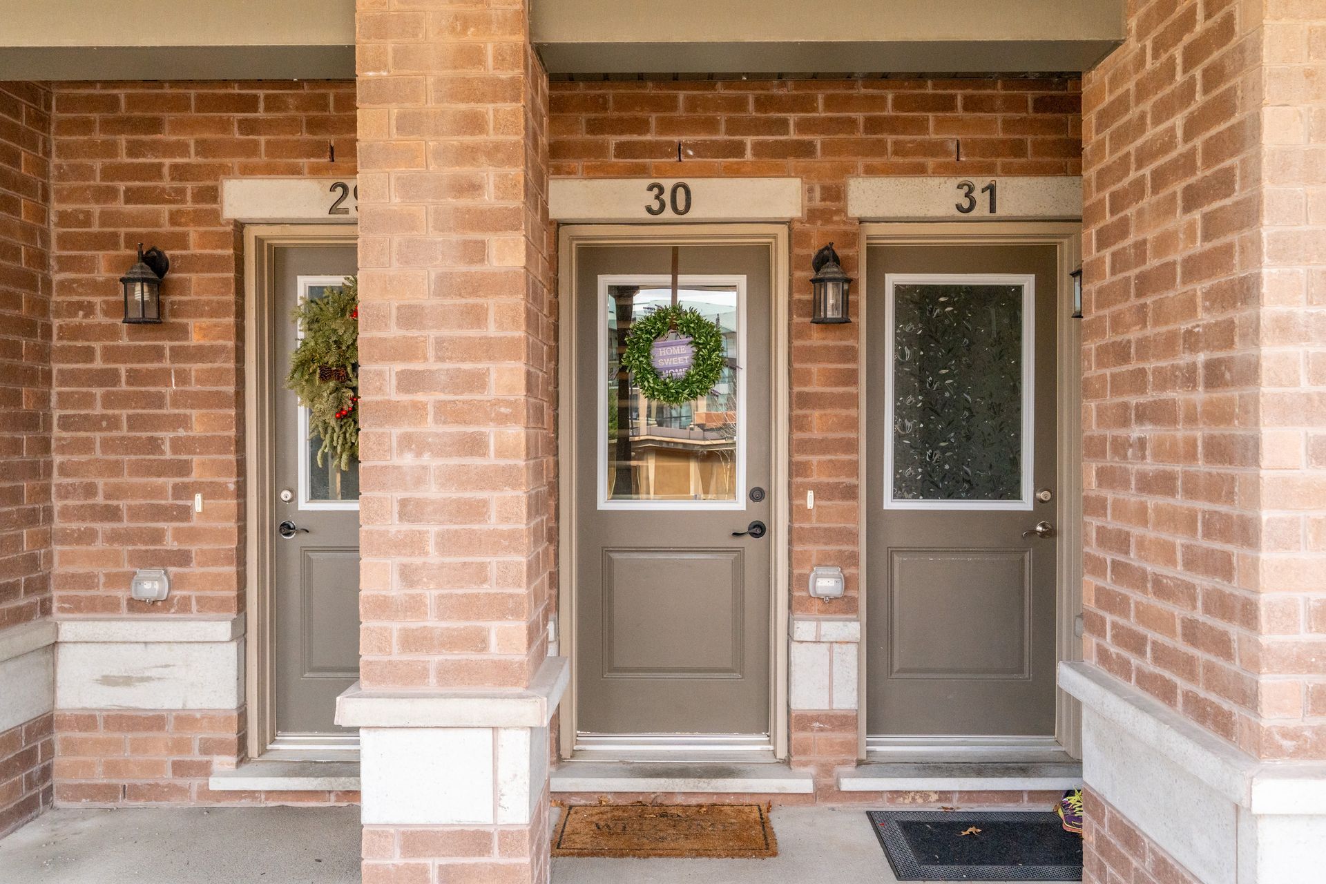 Row of brick townhouse entrances with numbers 29, 30, and 31, each with a front door and wreaths