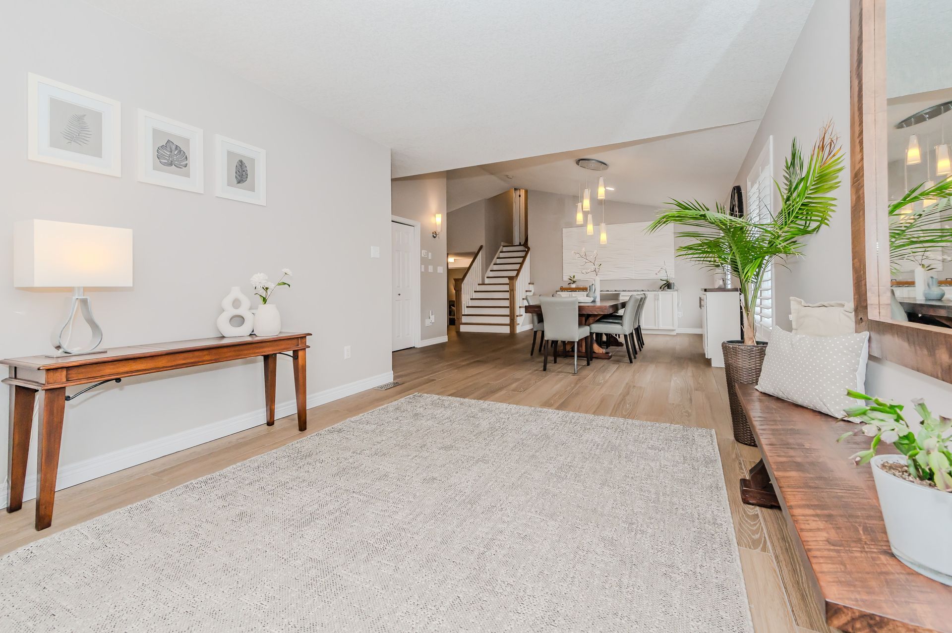 Bright modern living room with white rug, console table, staircase, and dining area beyond.