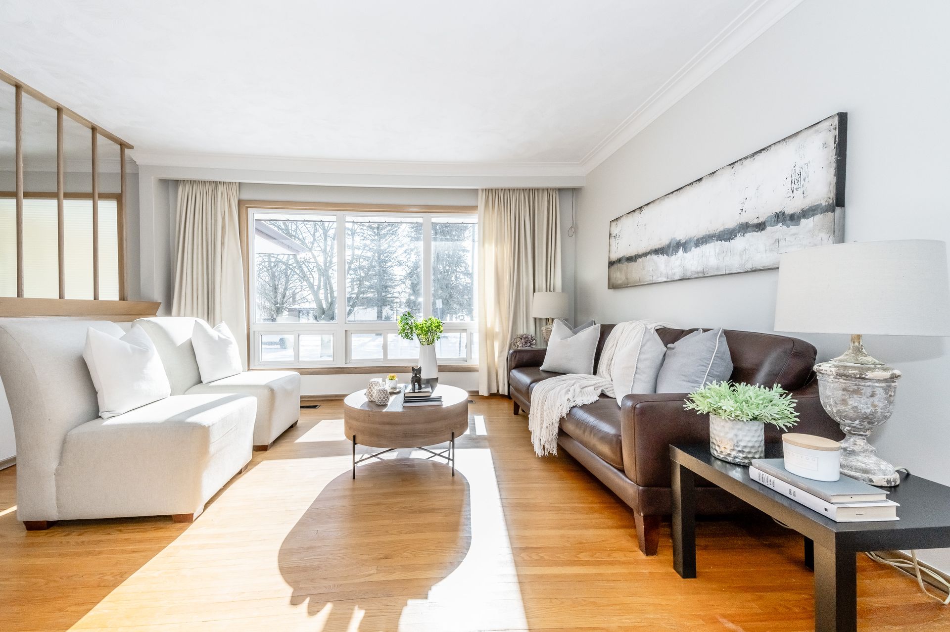 Bright living room with white and brown sofas, large window, and wooden floor