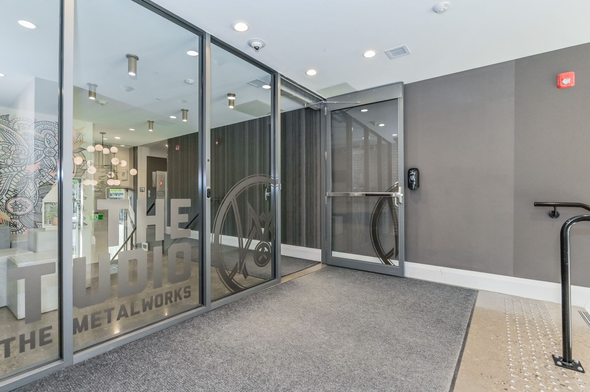 Glass office entrance with frosted logo, double doors, gray walls, and wheelchair-accessible ramp entrance