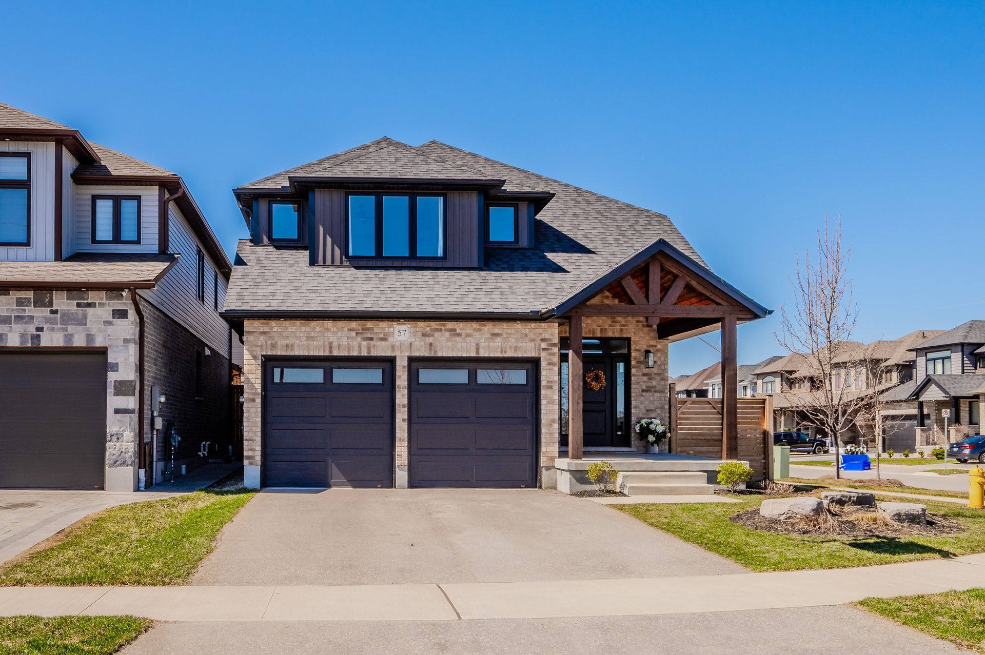 Modern suburban house with a double garage, stone facade, and front lawn under a clear blue sky