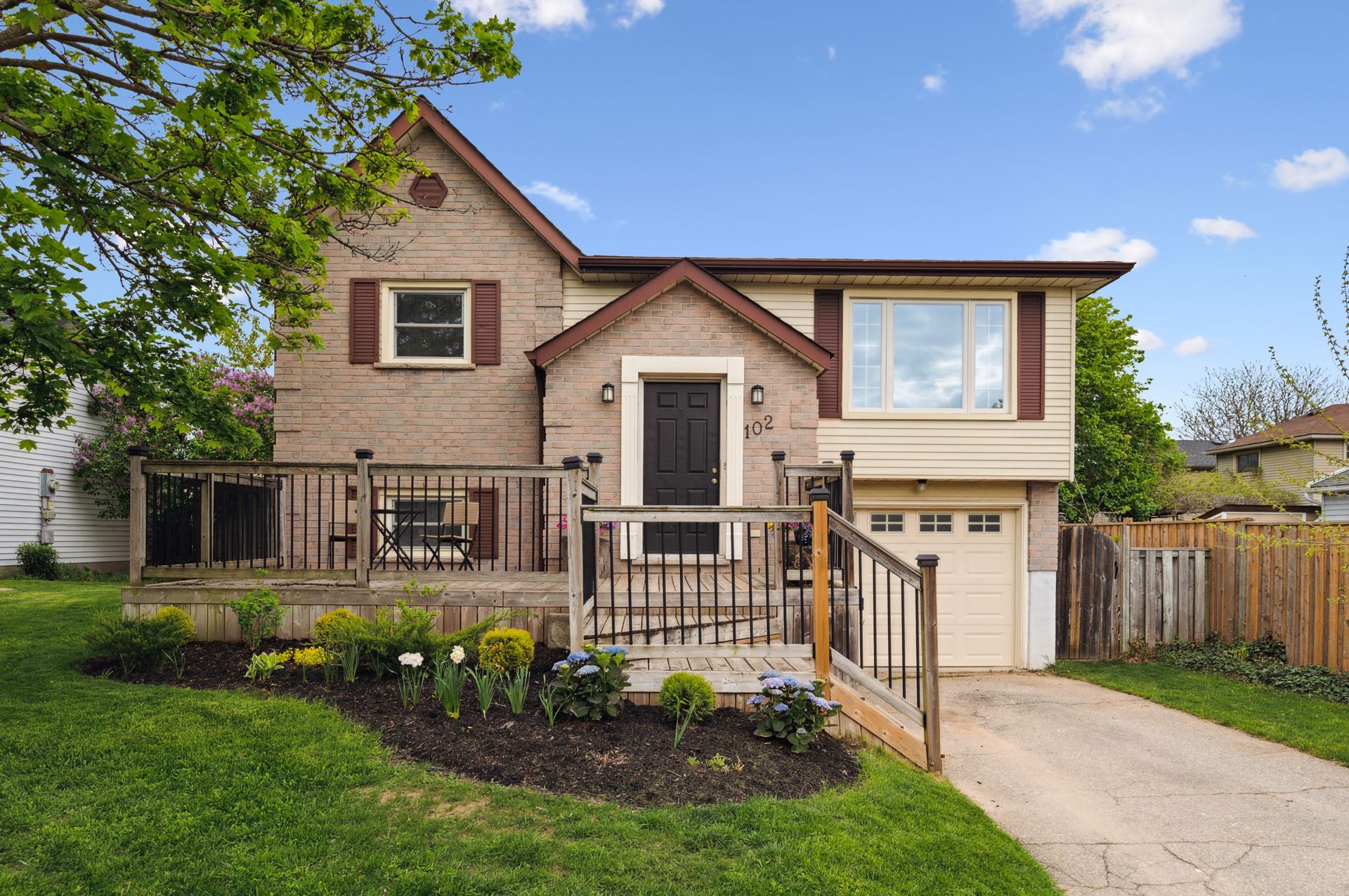 Two-story brick house with front porch, garage, and driveway in a landscaped suburban yard