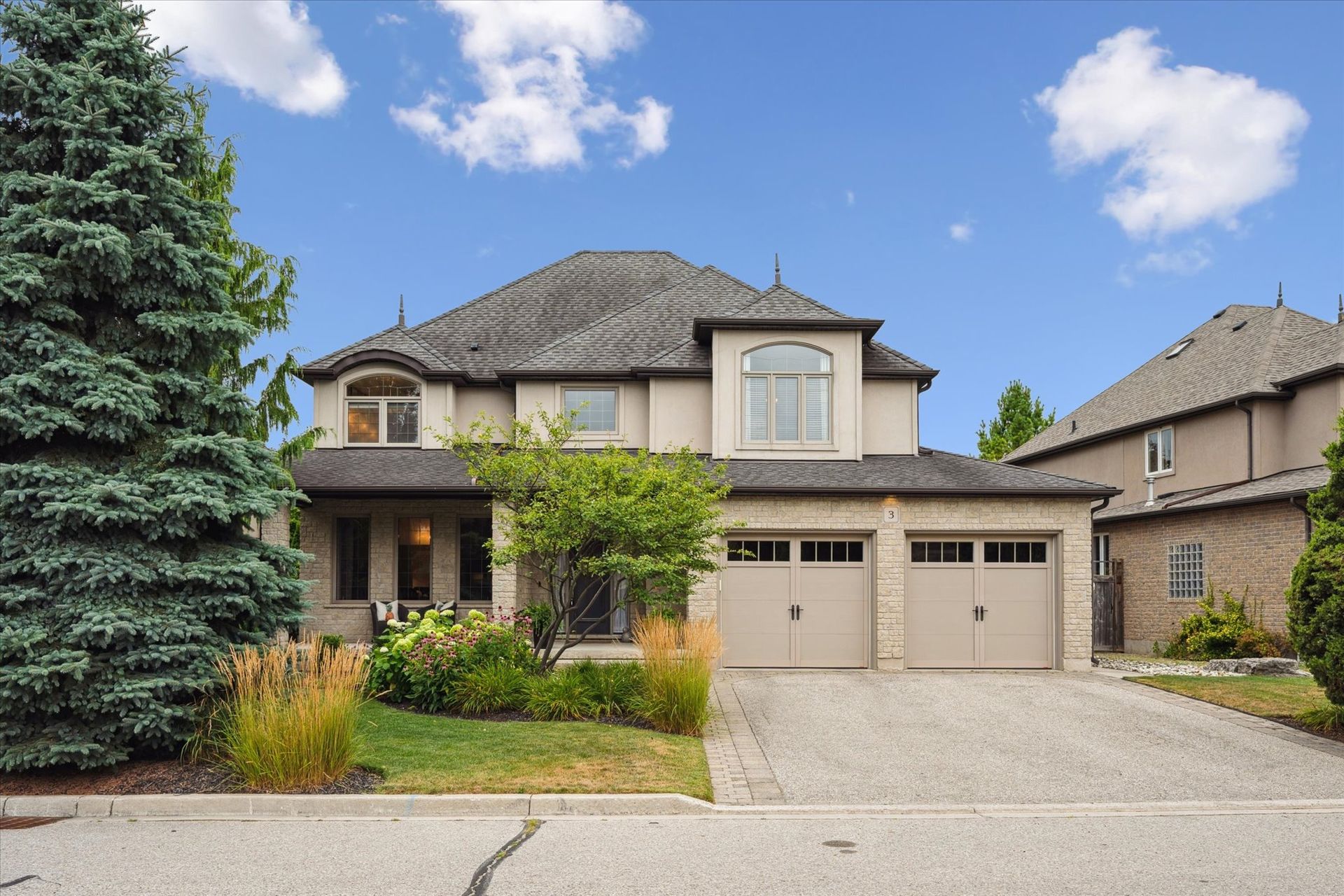 Two-story suburban house with a double garage, front porch, and large evergreen tree by the driveway.