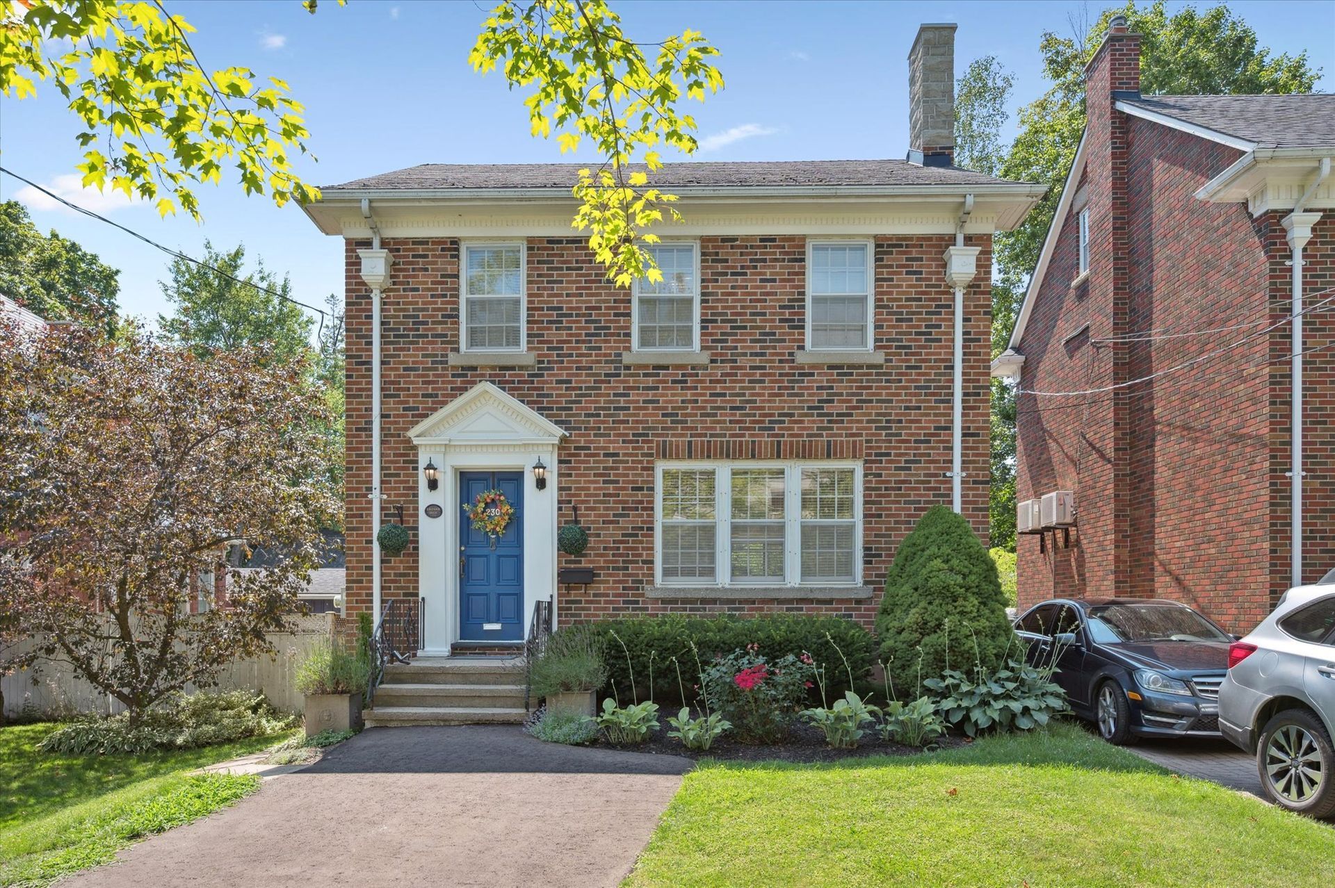 Two-story brick house with blue front door, front lawn, and parked cars on a sunny day