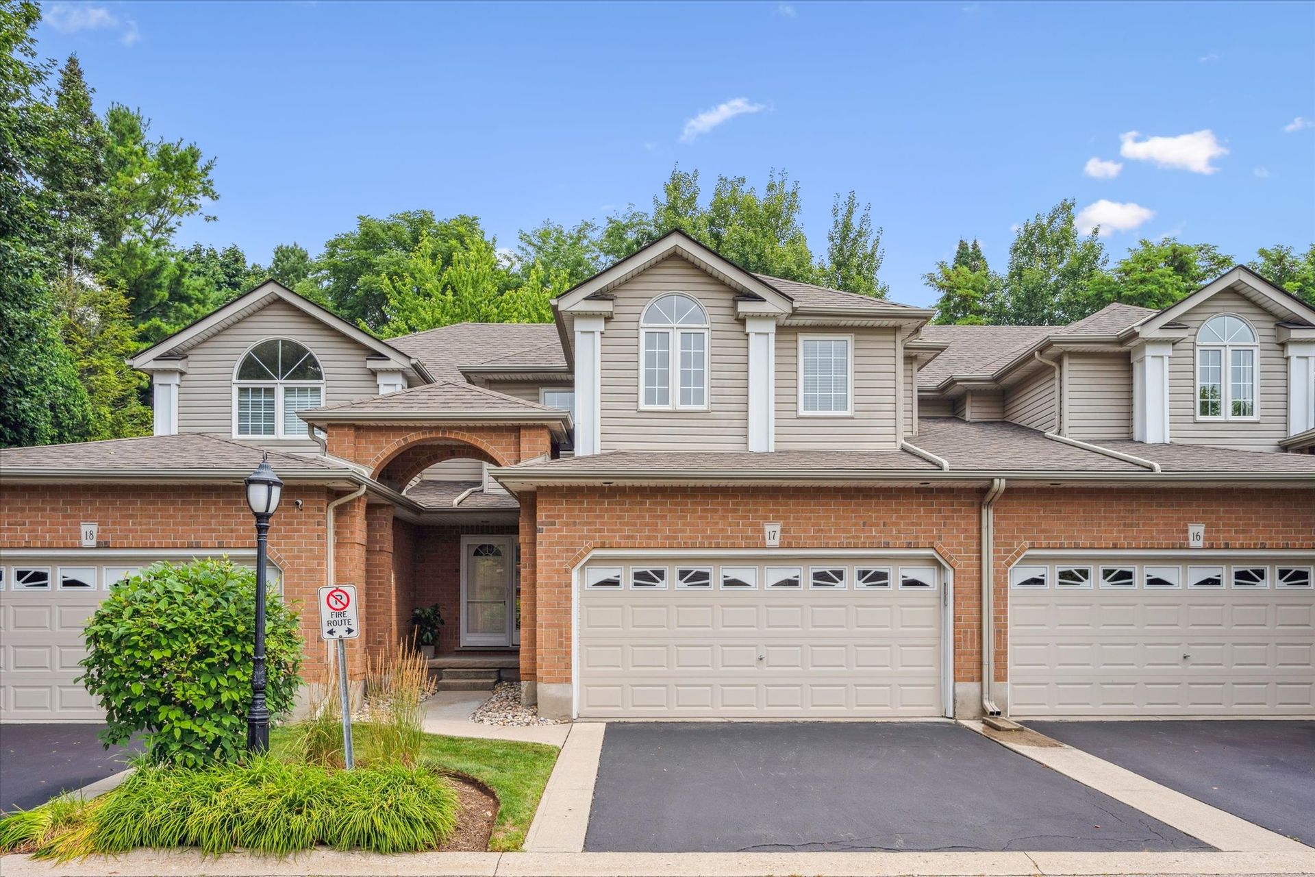 Row of beige brick townhouses with double garage doors and paved driveways under a blue sky