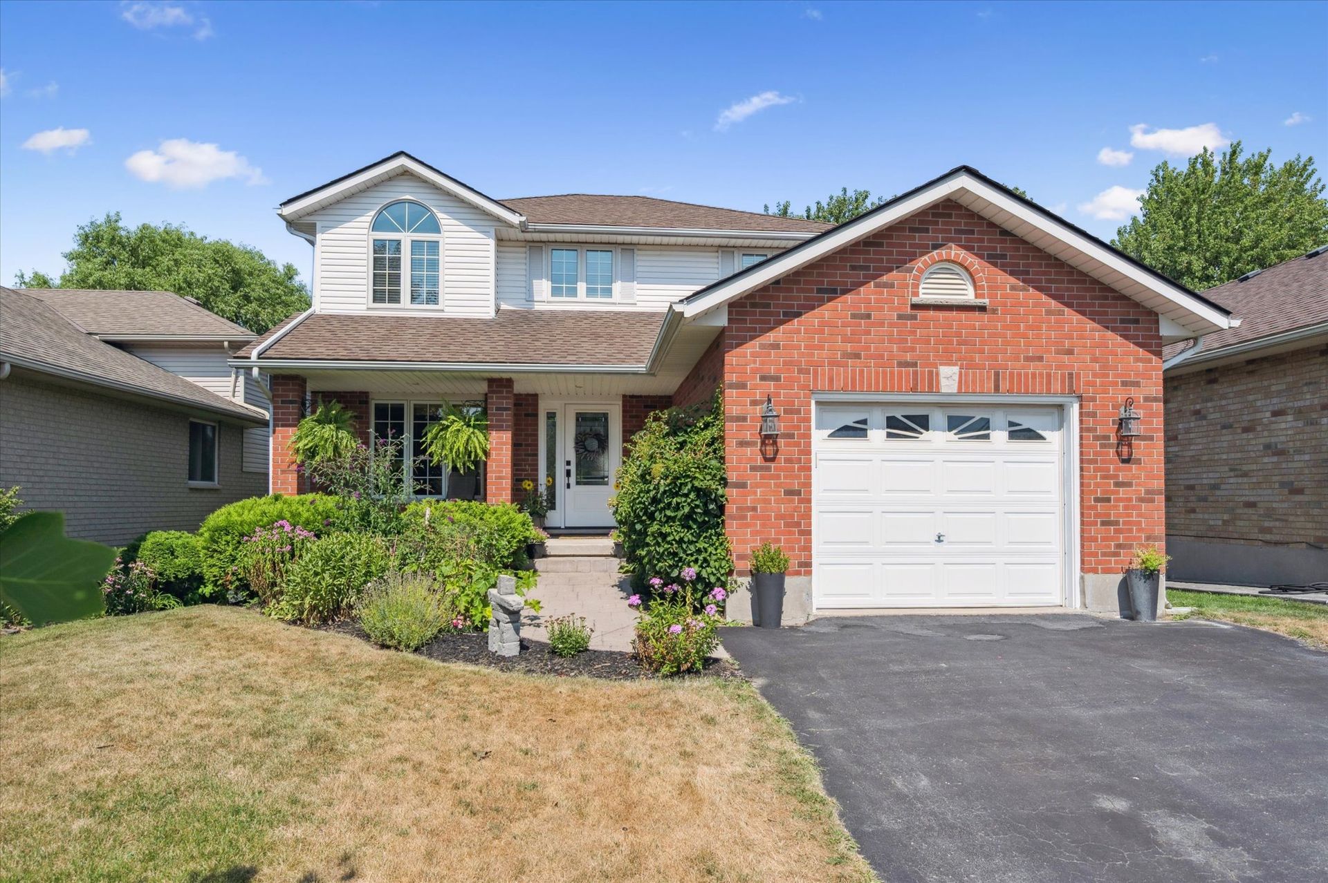 Suburban two-story brick house with white garage, front porch, and driveway under a blue sky