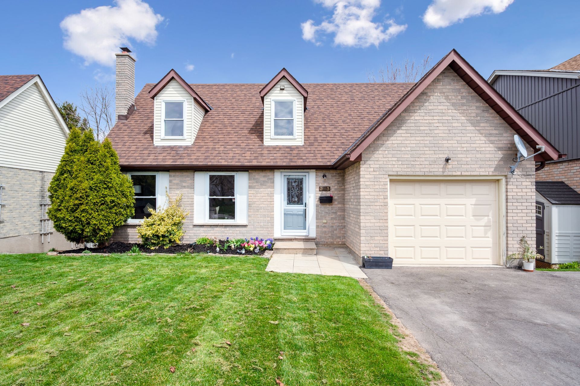 Suburban brick house with a two-car garage, front lawn, and blue sky.