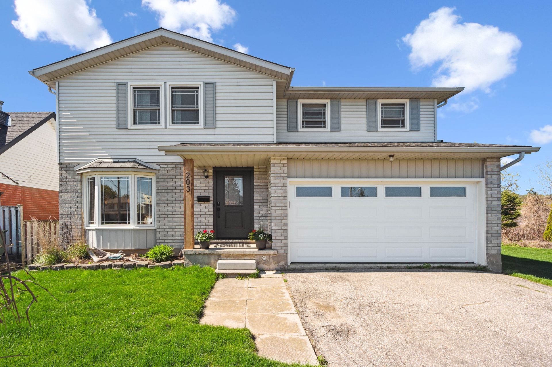 Two-story suburban house with a front lawn, driveway, and attached two-car garage under a blue sky