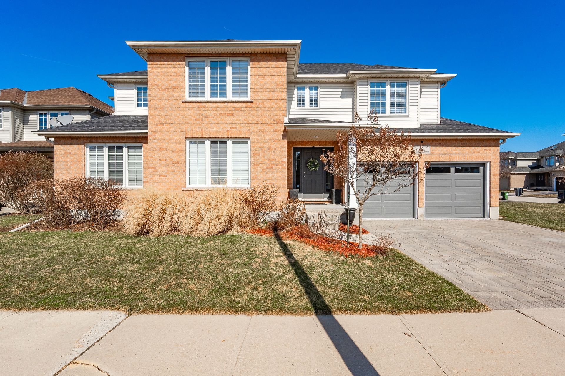 Two-story brick house with a garage and small front lawn on a sunny day