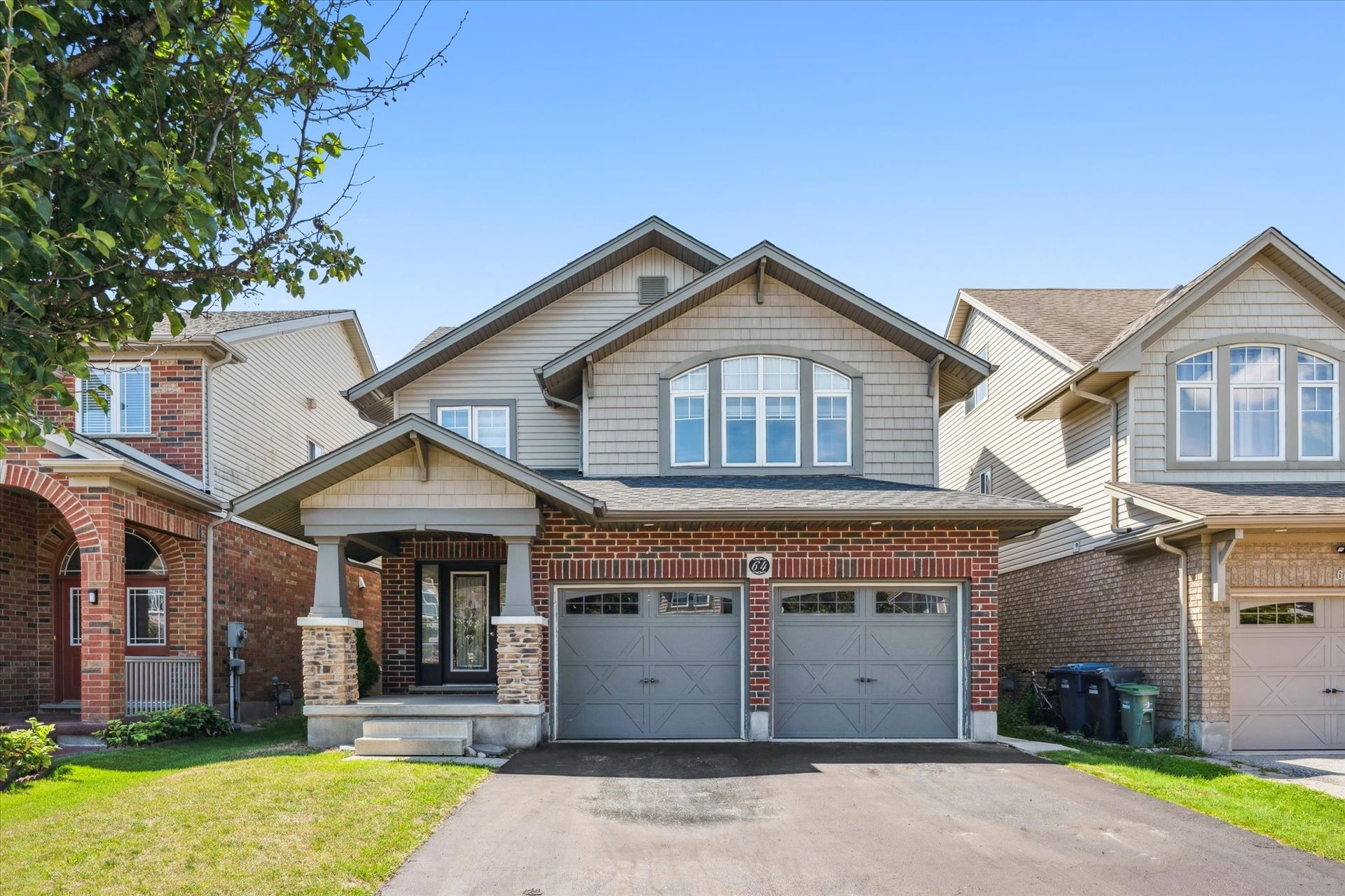 Suburban two-story house with stone accents, gray garage doors, and a driveway in front
