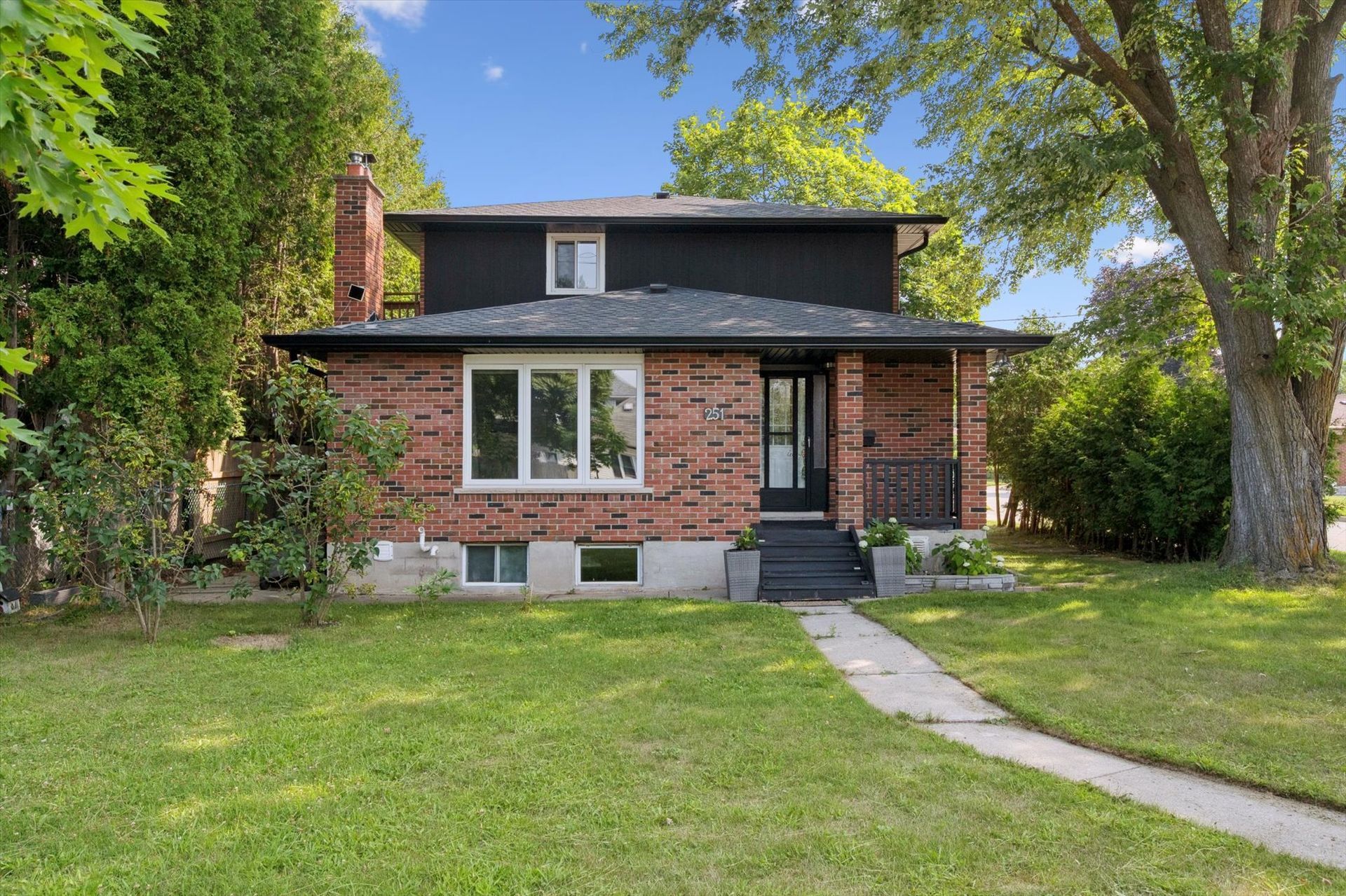Brick house with black roof, front porch, and large green lawn under trees