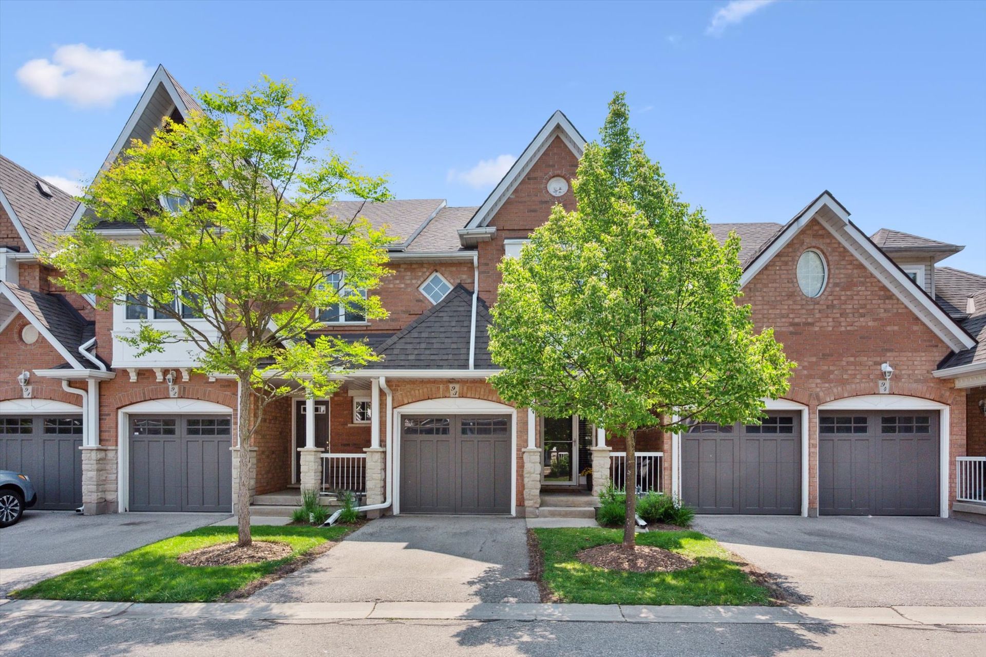 Row of brick townhouses with attached garages and small trees under a blue sky